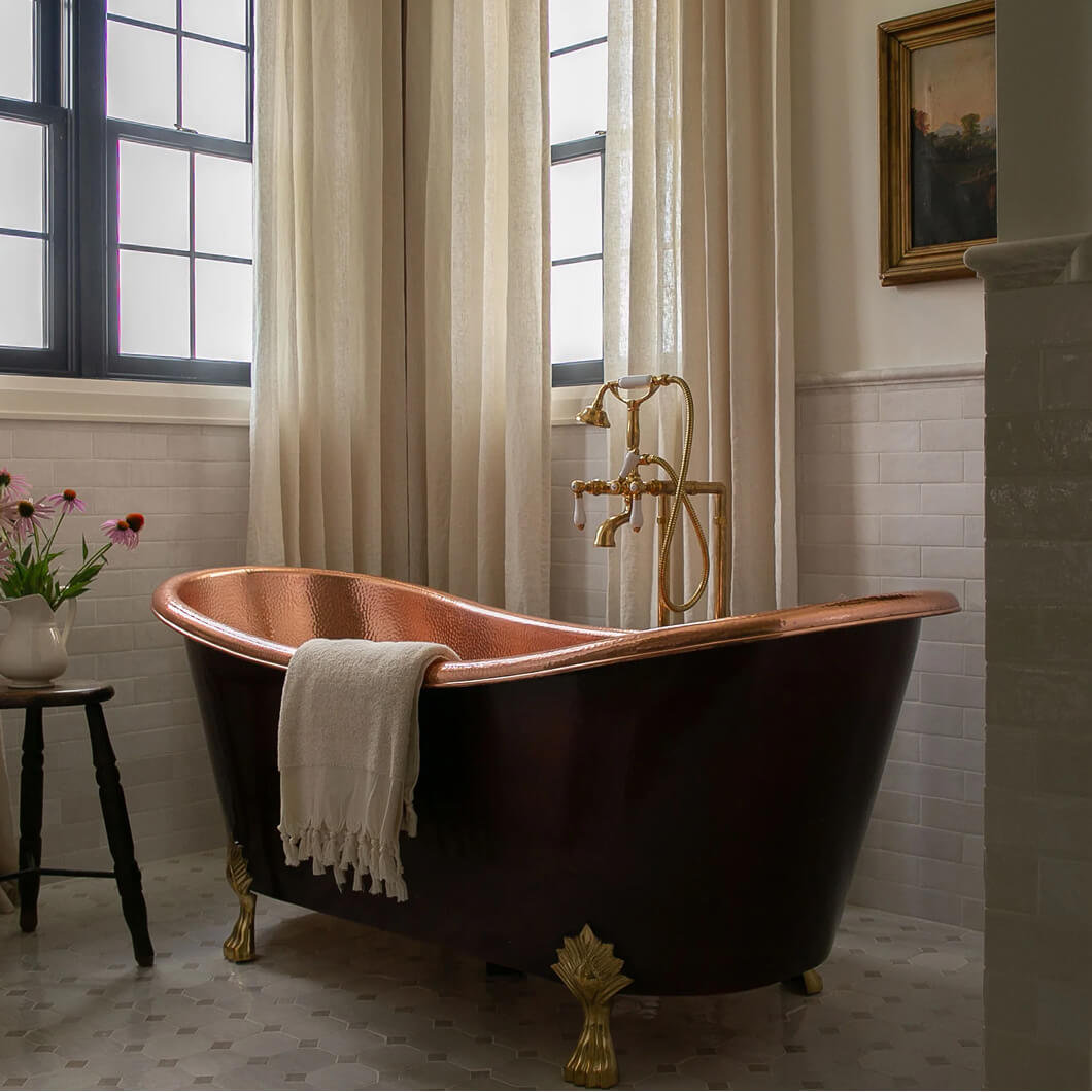 Copper clawfoot bathtub with a linen towel beside a curtained window