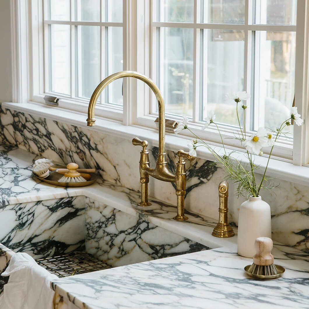 Marble kitchen sink with brass fixtures, a stone soap dish and fresh stems in a vase