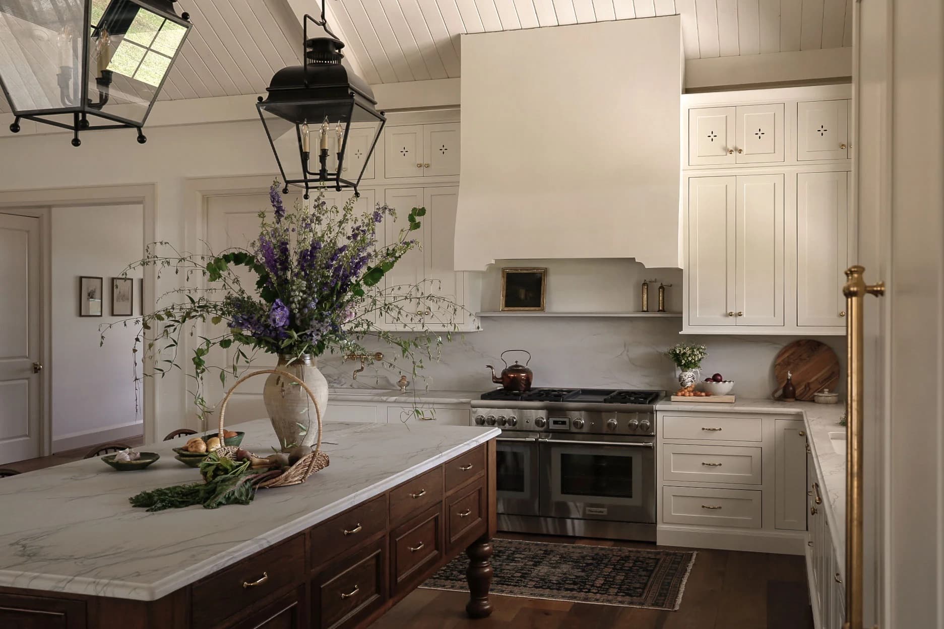 Kitchen island with a vase of purple delphiniums and a basket of bread beneath iron lanterns