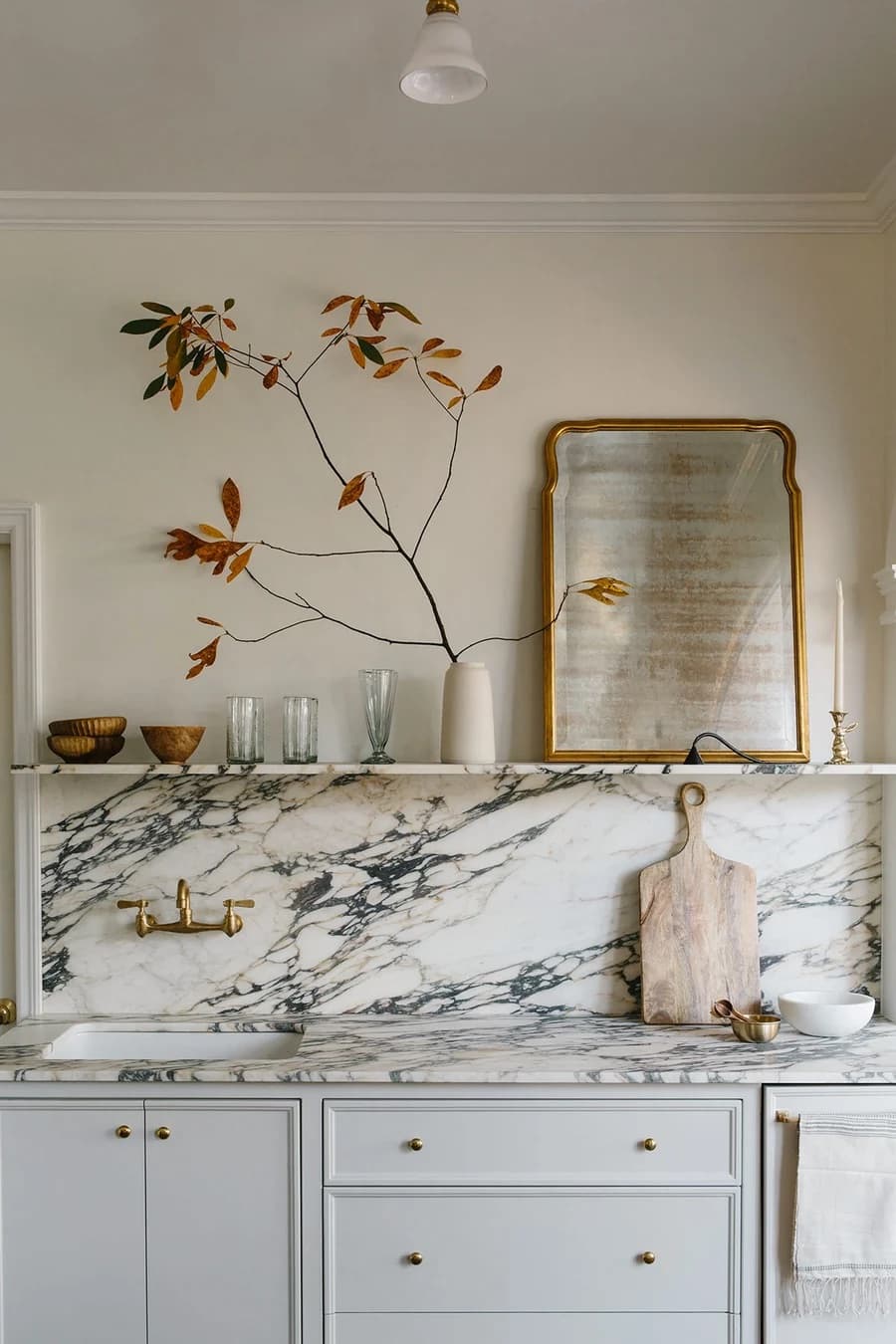 Marble backsplash with a brass shelf holding bowls, a vase of branches and a gilt mirror